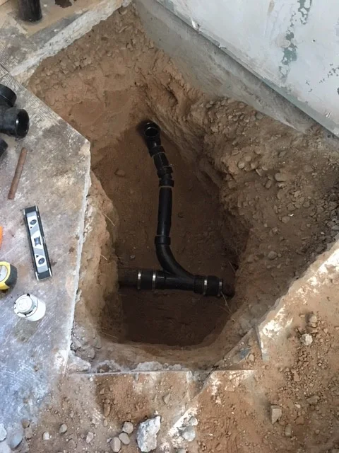 New PVC drain line and sanitary tee installed in an excavated slab pit