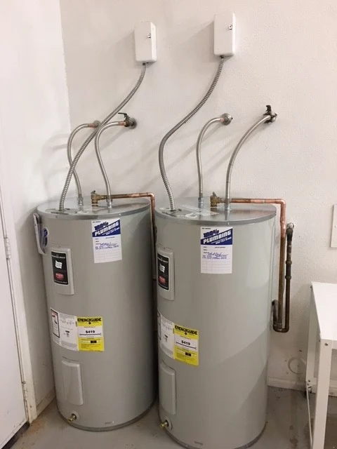 Two new electric water heaters installed side by side with braided supply lines