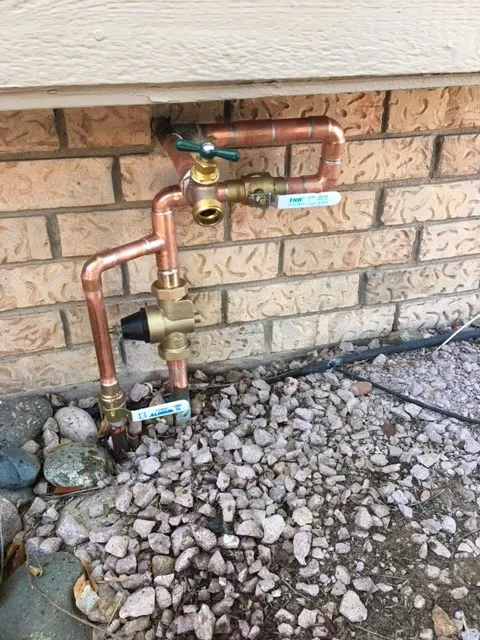 Exterior copper main shut-off and backflow assembly mounted to a brick home