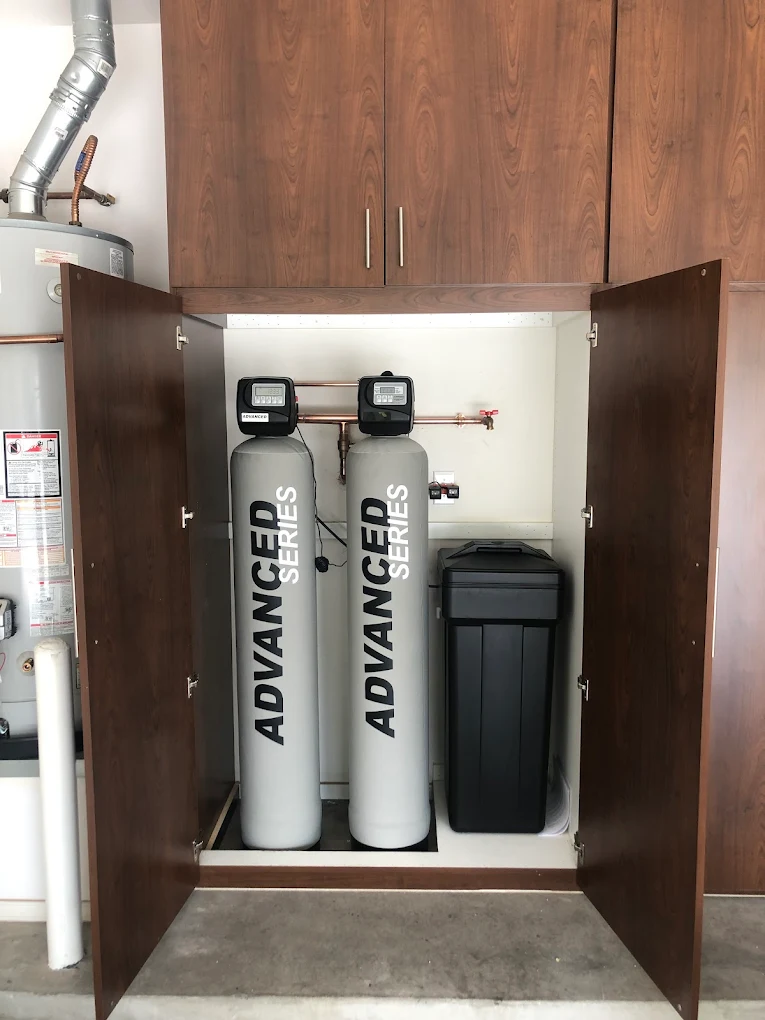 Twin Advanced Series water softeners neatly installed inside a custom wood cabinet